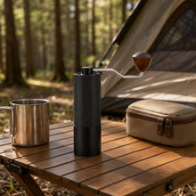 Slow Mill Manual Coffee Grinder Pro packed for camping on an outdoor table with a stainless steel cup and carry case